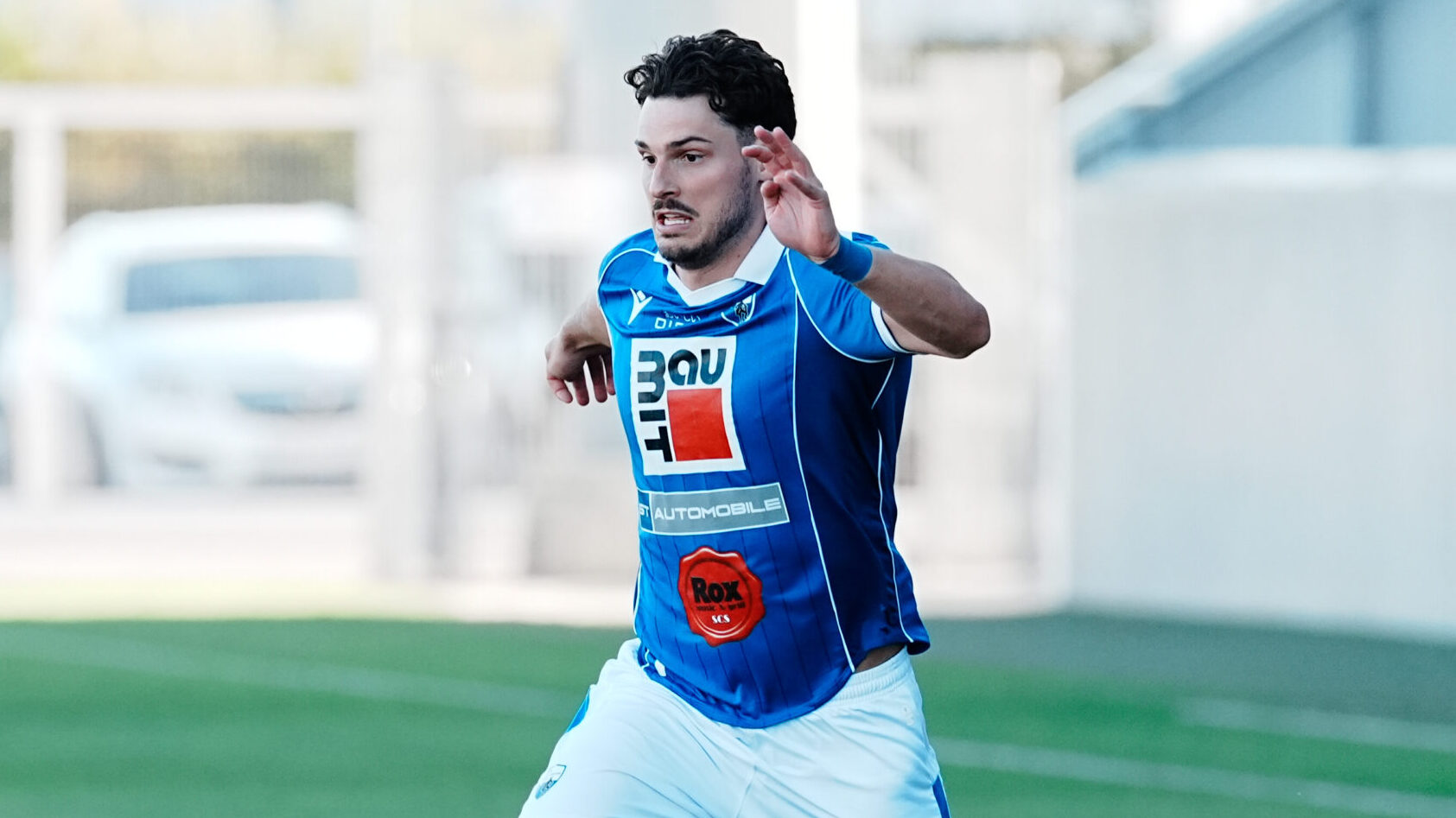 Fußballspieler im blauen Trikot mit Sponsorenlogos am Rasen